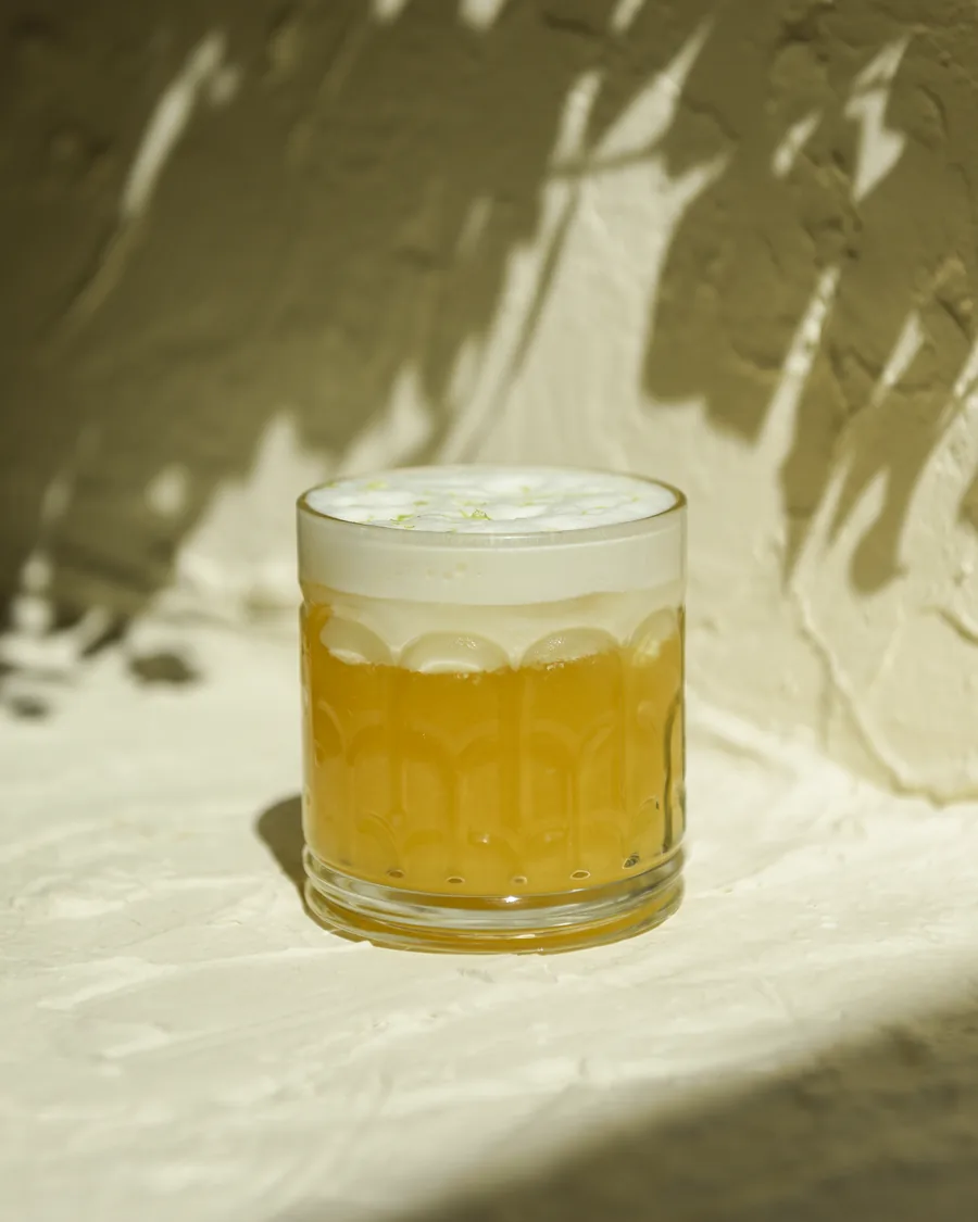 Cocktail maison mousseux dans un verre ciselé, sous une ombre de palmier